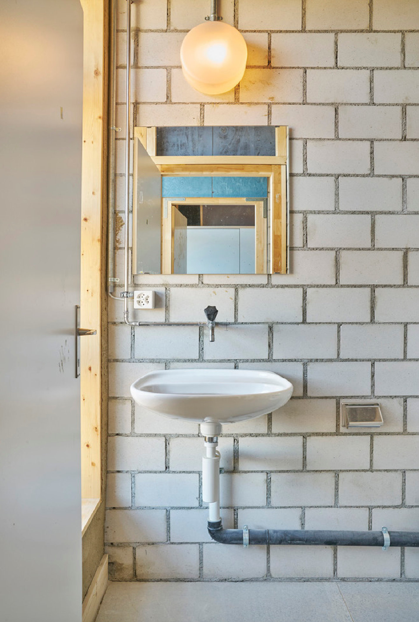 Wiederverwendetes Lavabo mit Spiegeln an Kalksandsteinwand